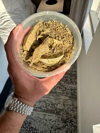 A tub of olive-tan ambergris flakes and powder held in hand