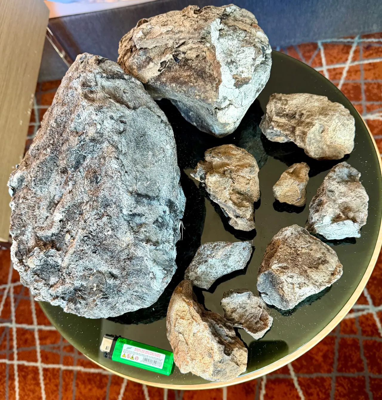 A large blue-grey ambergris piece, a second large piece and eight small ones on a round black table, a lighter for scale
