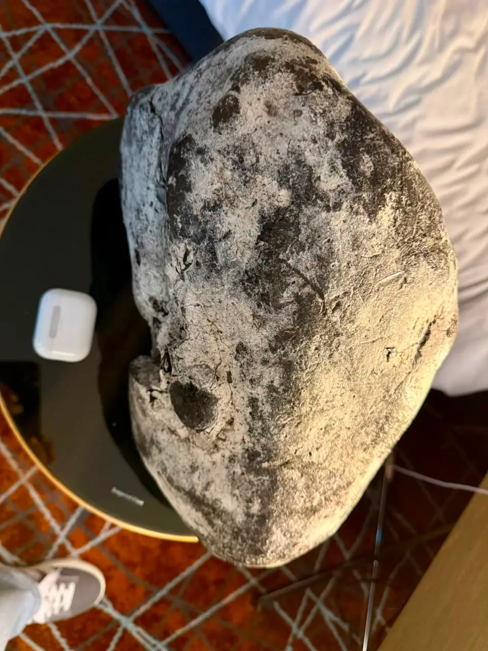A large pale grey ambergris piece with black blotches on a black table, an earbud case beside it