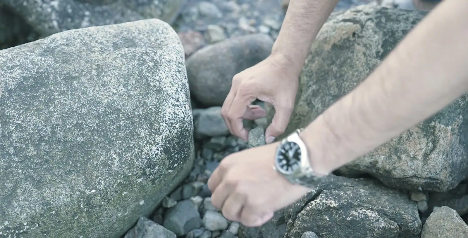 A hand reaching between shore rocks to check a possible find