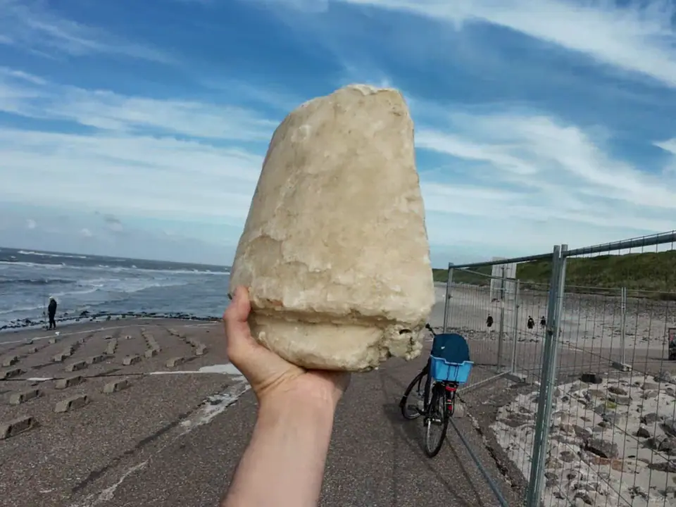 A pale slab of washed-up paraffin wax held up on a beach