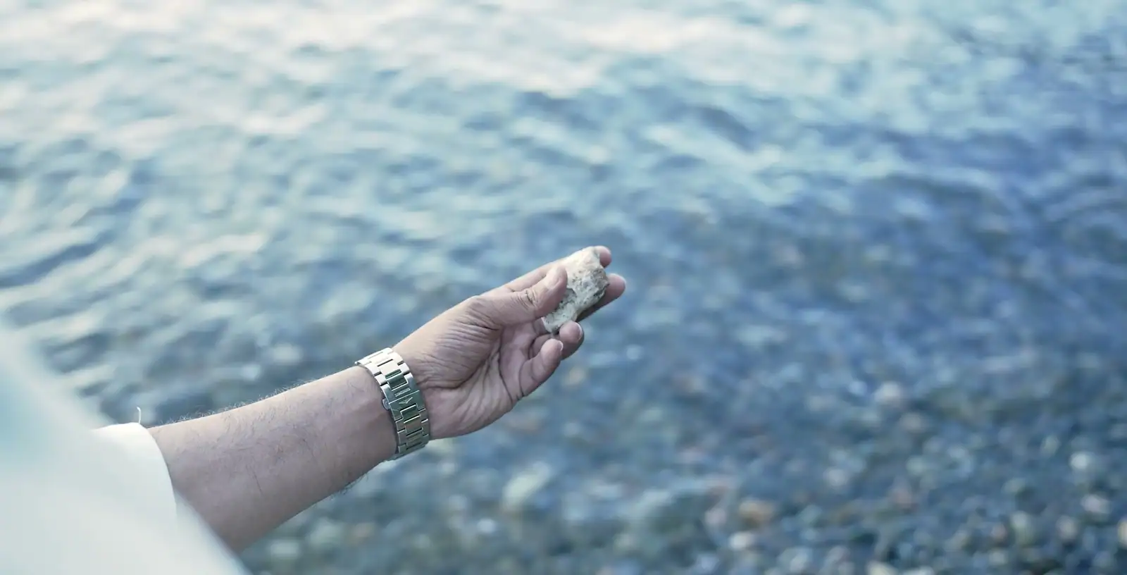A hand holding a small pale piece of ambergris over calm blue sea water