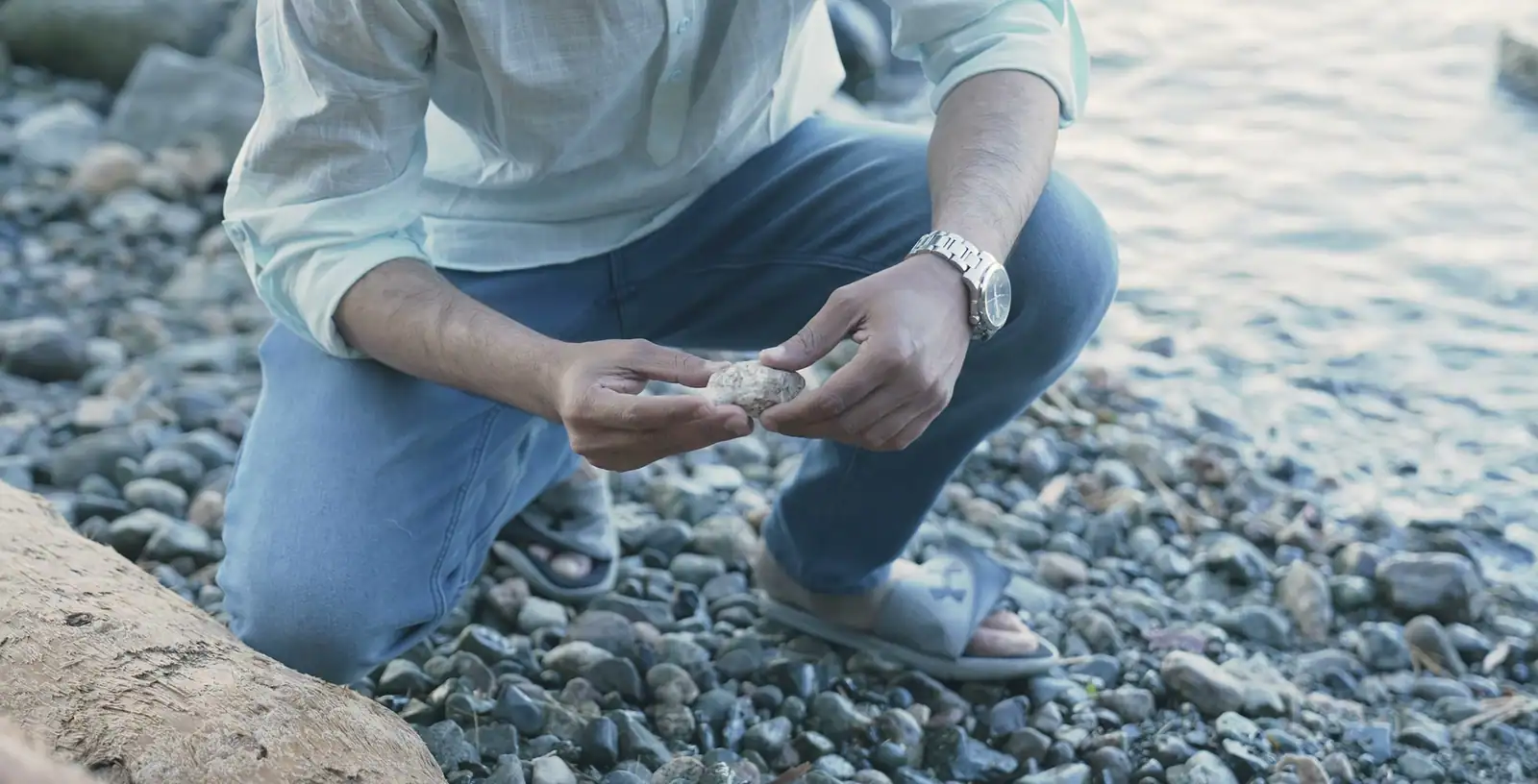 Nabil Valiulla crouched on a pebble beach, holding a small pale piece of ambergris in both hands