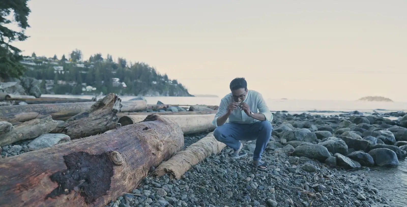 Nabil Valiulla crouched on a driftwood beach, examining a piece of ambergris