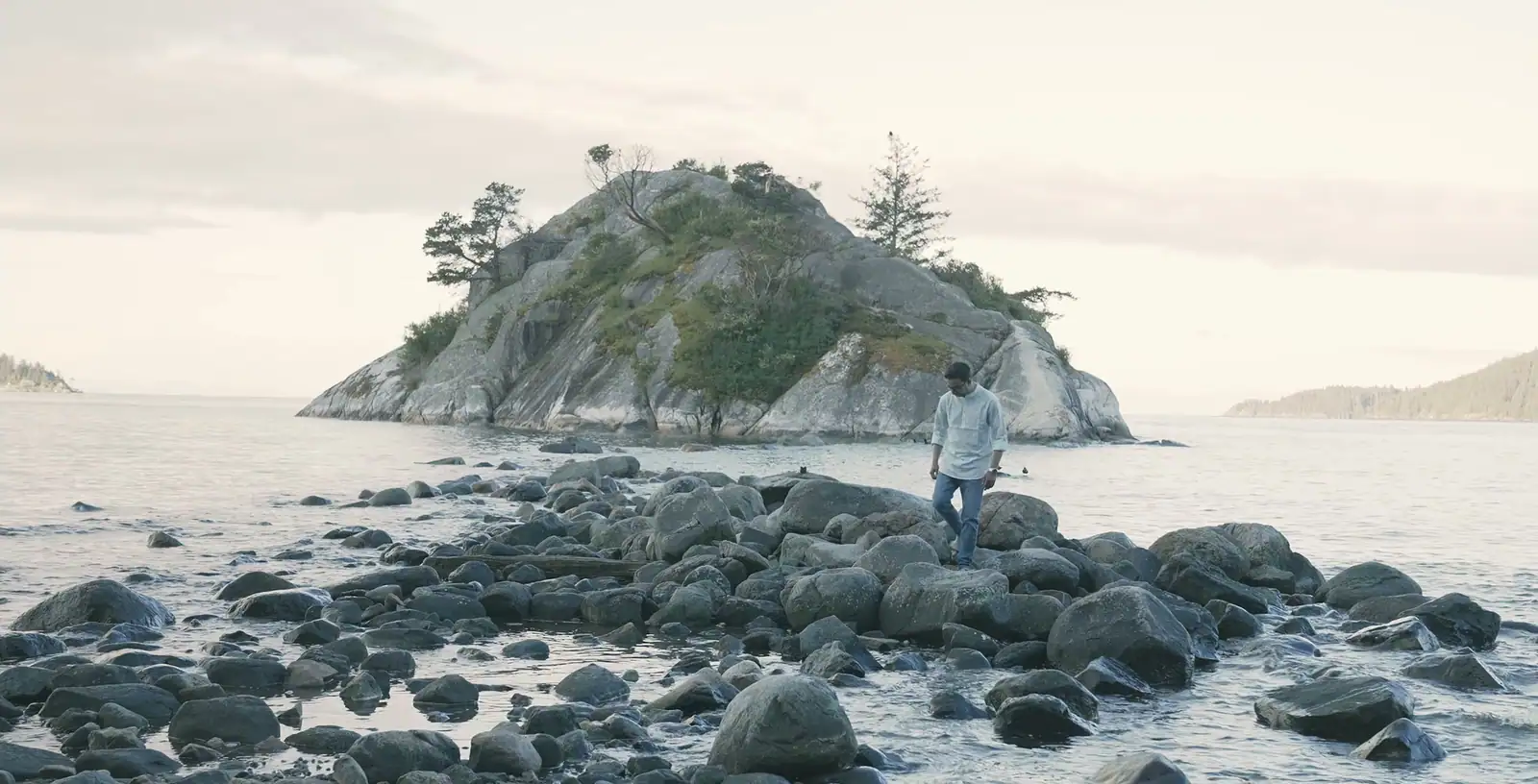 Nabil Valiulla walking over shore boulders in front of a small wooded island