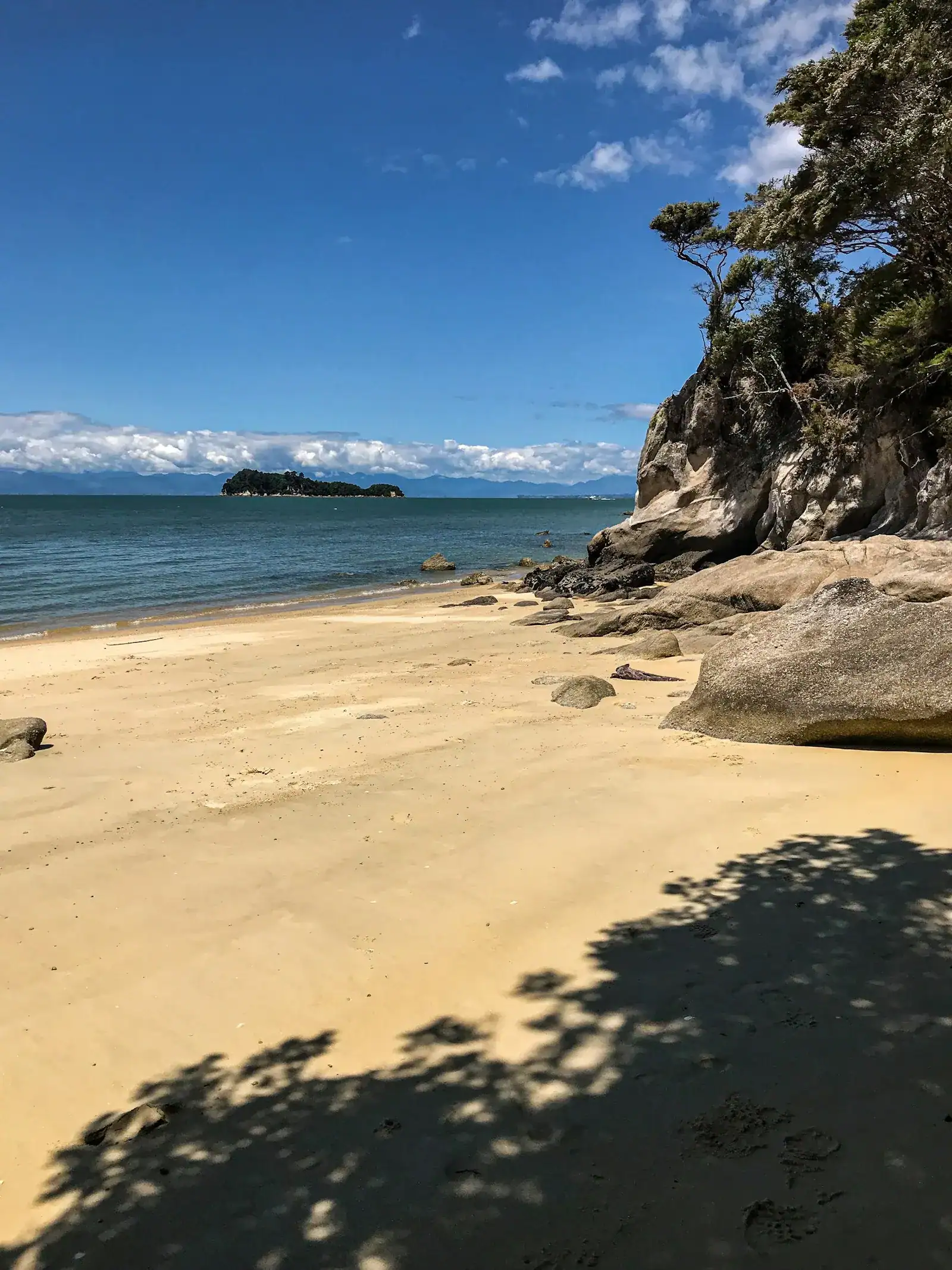 A golden sand cove with granite boulders and a small island offshore, New Zealand