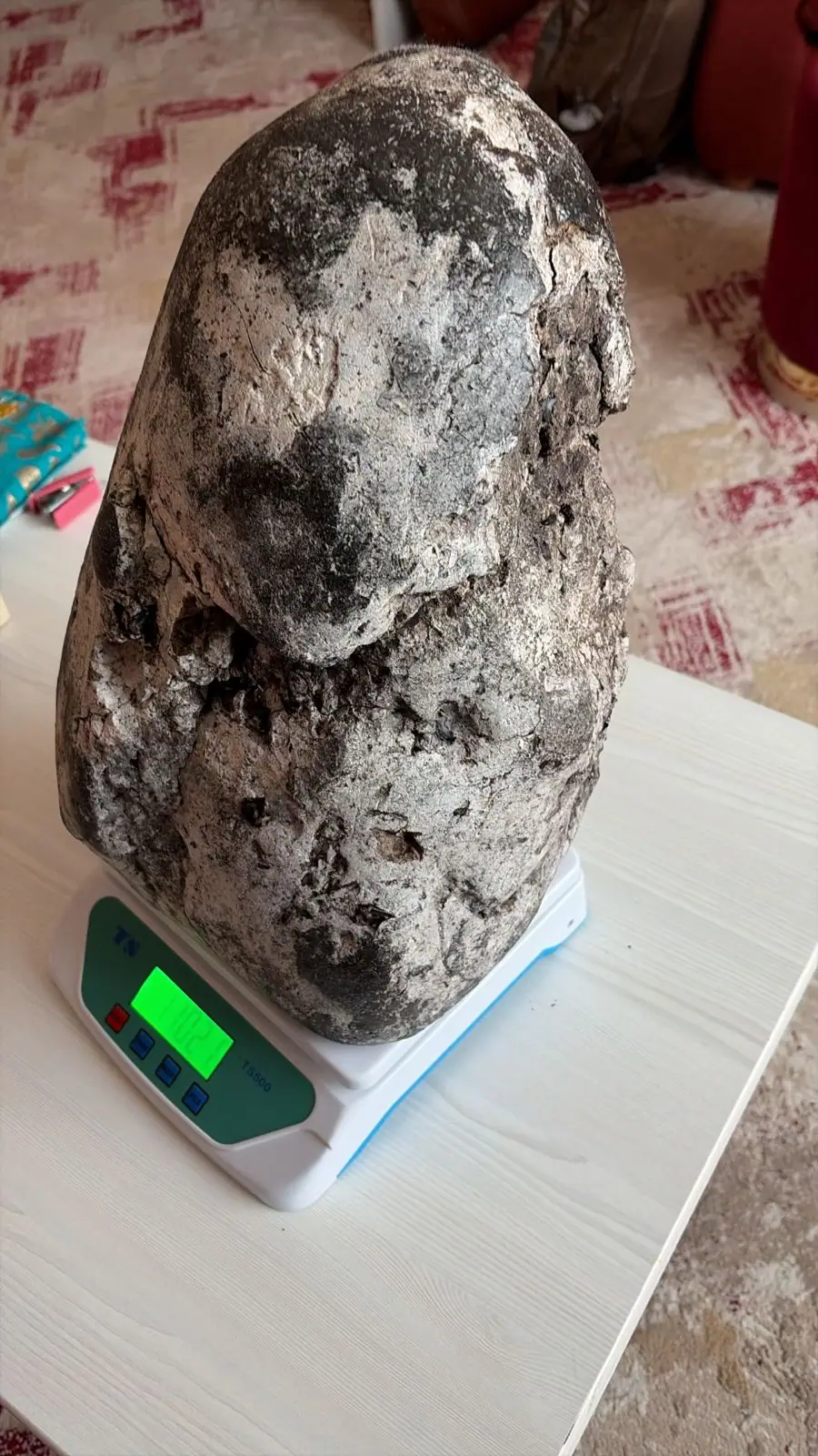 A tall black and white mottled ambergris piece standing on a white digital scale