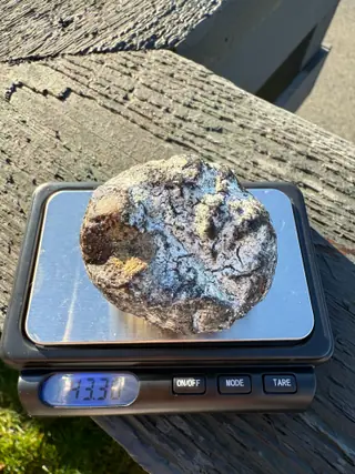 The round white-crusted ambergris piece on a small silver pocket scale on a deck rail